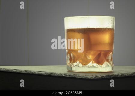 Misted glass with drops of water and whiskey with ice. Sweaty glass of whiskey with ice on table with copy space Stock Photo