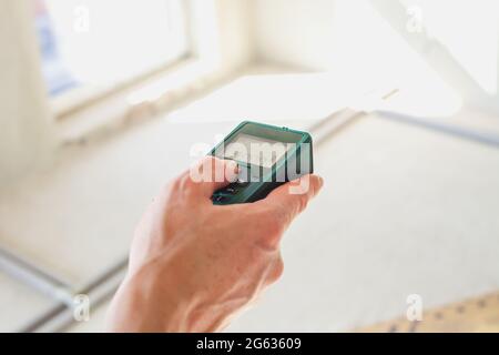 Laser rangefinder in man hand. Engineer holding laser distance meter. Close up measuring device in house. Worker using electronic range finder on buil Stock Photo