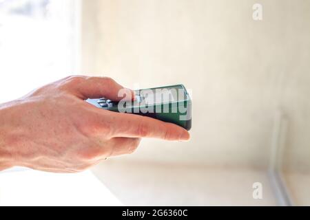 Laser rangefinder in man hand. Engineer holding laser distance meter. Close up measuring device in house. Worker using electronic range finder on buil Stock Photo