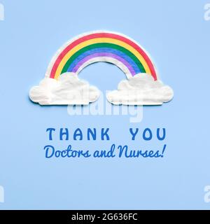 Rainbow with clouds. Text Thank you doctors and nurses. Many thanks to NHS fighting pandemics. Motivation square flat lay on light blue background. Stock Photo