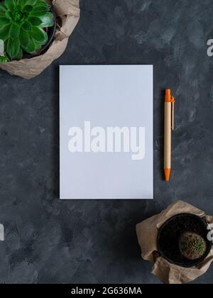 White blank notebook mockup dark background flat lay. Minimal work space sketchbook template, eco paper pen, green plant top view. Back to school bann Stock Photo
