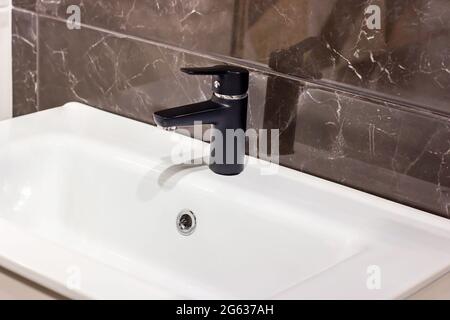 New modern black water faucet with the white sink on the ceramic tile wall background in the bathroom. Stock Photo