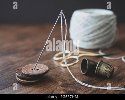 Pile of wooden buttons, needle, old thimbles, scissors and a cotton thread reel on the table. Concept of needlecraft, sewing, tailoring Stock Photo