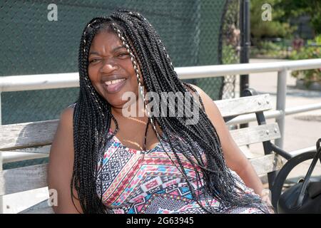 Posed portrait of a cheerful laughing attractive Nigerian American woman with long hair extensions. In Brighton Beach, Brooklyn, New York City. Stock Photo