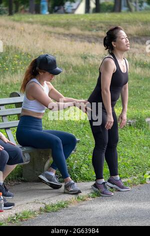 A woman working with her trainer on the proper form for deep knee bend exercises. I a park in Queens, New York City. Stock Photo