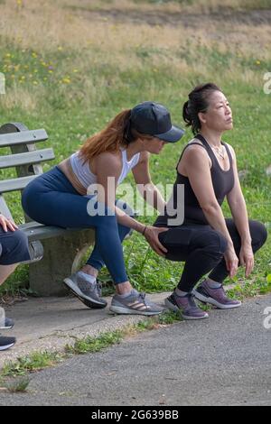 A woman working with her trainer on the proper form for deep knee bend exercises. I a park in Queens, New York City. Stock Photo