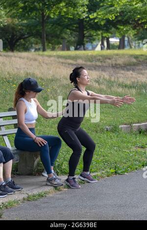 A woman working with her trainer on the proper form for deep knee bend exercises. I a park in Queens, New York City. Stock Photo