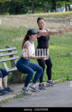 A woman working with her trainer on the proper form for deep knee bend exercises. I a park in Queens, New York City. Stock Photo