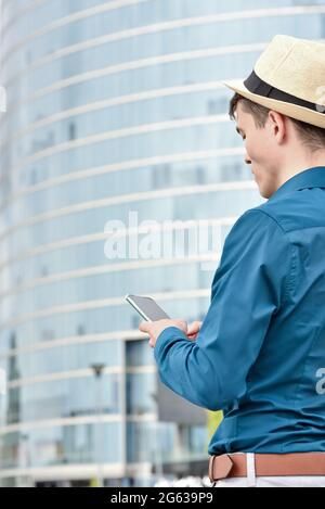 Young man looks at a smartphone, texting and talking while working and communicating on the Internet. Using mobile technologies for remote work. Stock Photo