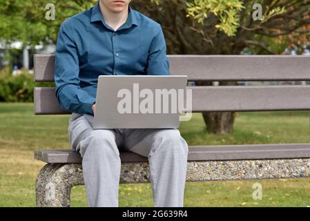 A student sits on a bench in a city park and uses a computer for online learning. A freelance programmer works remotely. Online communication and remo Stock Photo
