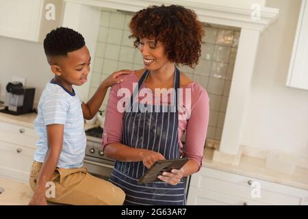 Happy african american mother with son baking in kitchen, using tablet Stock Photo