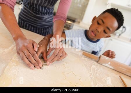 Happy african american mother with son baking in kitchen, cutting cookies Stock Photo