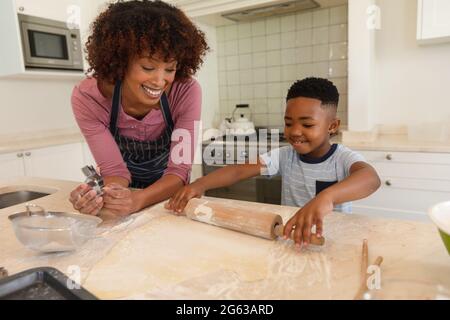 Happy african american mother with son baking in kitchen, rolling dough Stock Photo