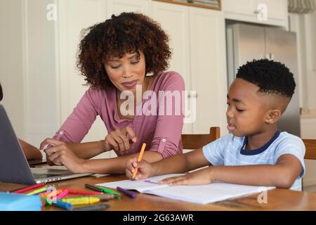 Happy african american mother and son doing homework at home smiling Stock Photo