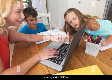 Caucasian mother using laptop and doing homework with her daughter and son smiling at home Stock Photo