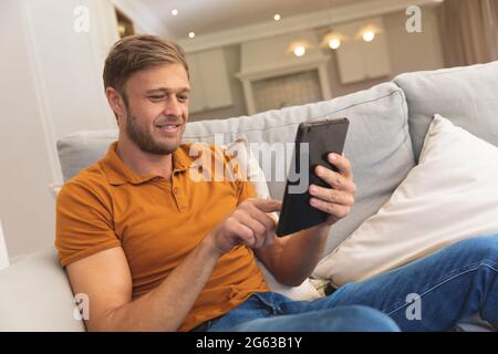 Caucasian man sitting on couch, smiling and using tablet at home Stock Photo