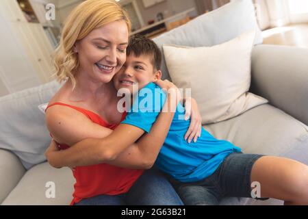 Caucasian mother and son sitting on couch embracing and smiling at home Stock Photo