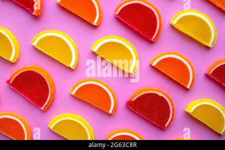 Colorful oval citrus jelly candies pattern on a pink background. Yellow, pink, red, orange round shaped marmalade pattern. Stock Photo