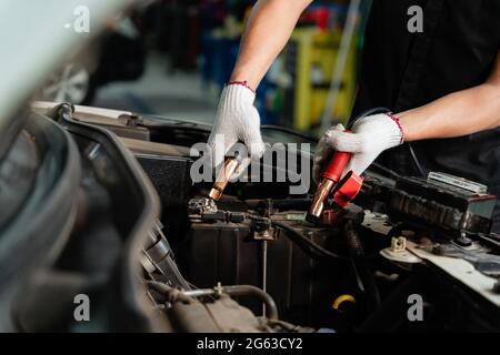 Close up hand of mechanic hand charging battery of a car with electricity through jumper cables, battery inspection Stock Photo