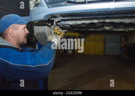 A gloved mechanic uses a key to align the curved part of the car's body. the machine is hanging on a hydraulic lift. Car service business concept Stock Photo