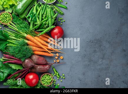 Fresh carrots, zucchini, peas, tomatoes and greens on a dark blue background. Top view, copy space. Stock Photo