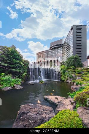 tokyo, japan - july 01 2021: Big waterfall with Japanese koi carps in the pond of the Hotel New Otani Japanese Garden at foot of the Hotel New Otani i Stock Photo