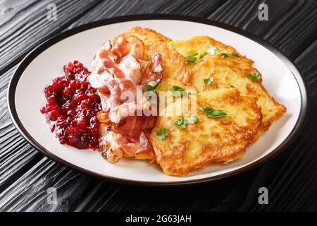 Crispy fried potato pancakes served with lingonberry jam and bacon close-up on a plate on the table. horizontal Stock Photo