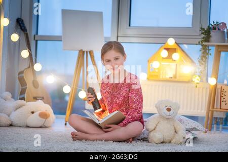 Little girl reading book with flashlight in evening room Stock Photo