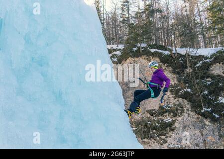 Woman climbing down the side of an icy slope, hanging on a rope attached to her harness Stock Photo