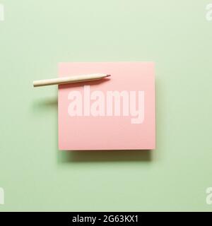 Blank pink memo pad with wooden pencil on green background. top view, copy space Stock Photo