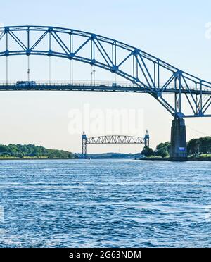 In the foreground, spanning the Cape Cod Canal, is the Bourne Bridge in Bourne, MA with the Cape Cod Canal Railroad Bridge in the distant background. Stock Photo