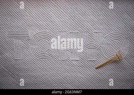 Japanese Zen garden raked with the word TOKYO in capital letters in textured white sand with diagonal stripe pattern and rake Stock Photo