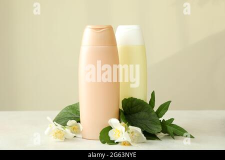 Blank bottles of shampoo and flowers against beige background Stock Photo