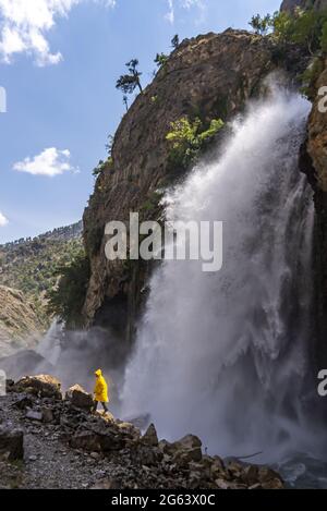 Vertical shot of a Kupusbasi waterfall in Turkey and a walking man with a yellow coat Stock Photo