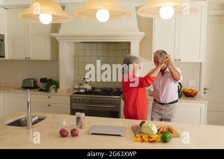 Senior caucasian couple dancing together and smiling in kitchen Stock Photo
