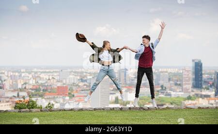 Cheerful young couple travelers in city on holiday, jumping. Cityscape in the background. Stock Photo