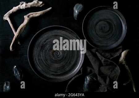 Empty black ceramic plates with black stones and wooden around on textile napkin over black wooden background. Flat lay. Stock Photo