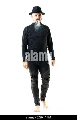 Authentic unique style artist in full black clothes and hat walking barefoot and smoking. Full body portrait isolated on white background Stock Photo