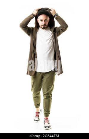 Stylish modern urban young man wearing cardigan put on hoodie walking towards camera. Full body portrait isolated on white background Stock Photo