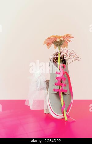 Vertical composition with trendy gray sneakers with gerbera and the bride's wedding accessory on a pink background with a copy space Stock Photo