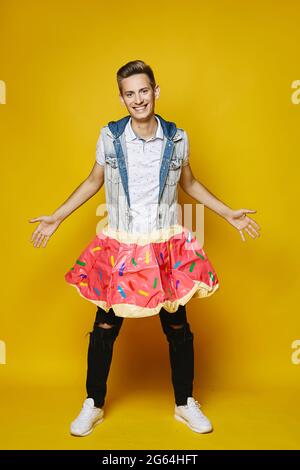 A young stylish blond man in a denim vest and black jeans smiles and looks at the camera, isolated at the yellow background. A young handsome guy in a Stock Photo