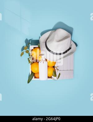 Natural cosmetic composition with citrus fruits in a wooden box, a white cosmetic bottle and summer hat on blue background. Summer cosmetics mock up Stock Photo