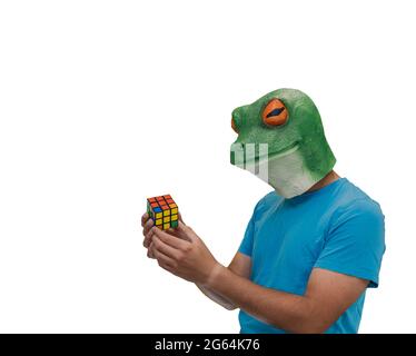 man with a frog mask on his head playing with a colorful puzzle called Rubik's cube on a white background and copy space Stock Photo