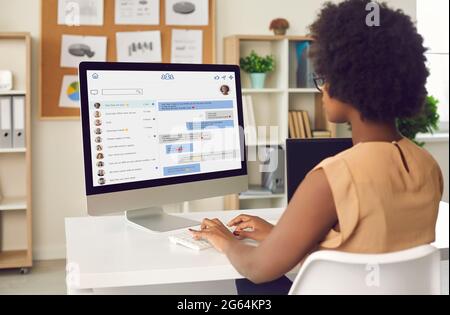 Black businesswoman sitting at office desk and messaging colleagues on work chat Stock Photo