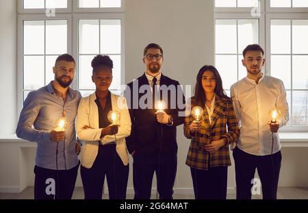 Group of young diverse business people standing in office holding shining light bulbs Stock Photo