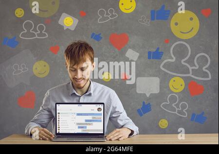 Happy young guy shows desktop version of new messenger app on laptop computer screen Stock Photo