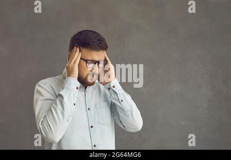 Worried adult caucasian man rubbing temple suffering from headache studio shot Stock Photo