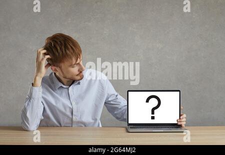 A man looks at a laptop screen with a question mark symbol. Stock Photo