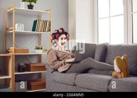 Young woman sitting on couch and looking at laptop with happy surprised face expression Stock Photo