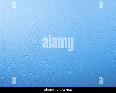 Close up raindrops and water runs on glass window pane surface over grey and blue sky background on rainy day Stock Photo